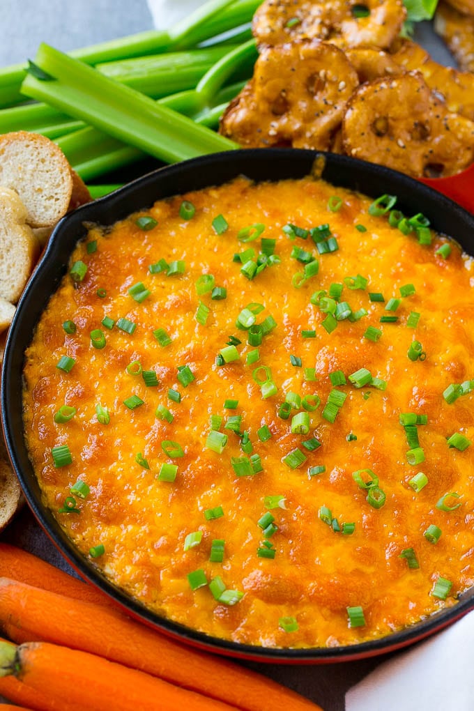 Buffalo Ranch Chicken Dip | Buffalo Chicken Dip | Baked Buffalo Dip | Cheesy Buffalo Dip #buffalowings #buffalochicken #dip #lowcarb #appetizer #fuyos Buffalo ranch chicken dip topped with melted cheese and green onions, surrounded by vegetables, pretzels and baguette slices.
