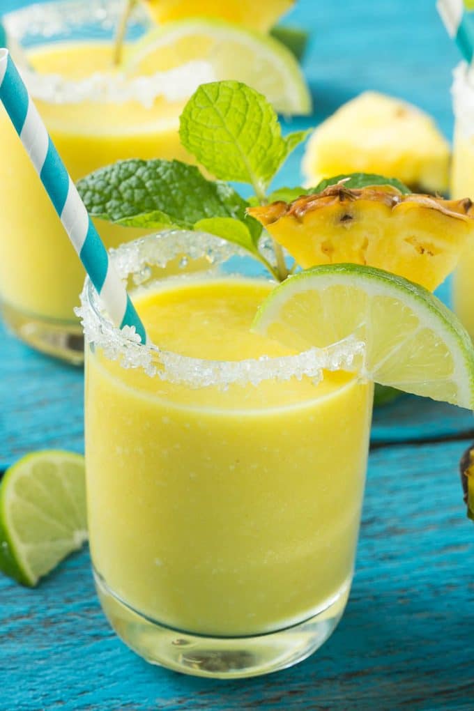 Pineapple Coconut Smoothie Recipe |Tropical Smoothie | Pineapple Smoothie #smoothie #pineapple #coconut #healthy #cleaneating #fuyos A cup of pineapple smoothie with garnishes of lime, pineapple wedges and mint sprigs.