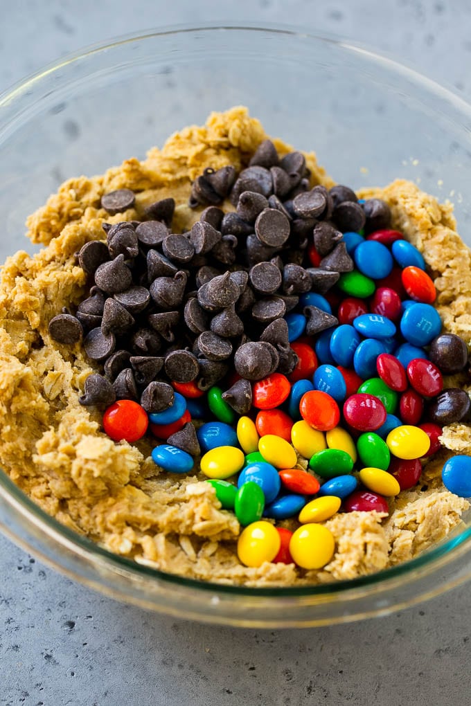 Monster Cookies Recipe | Oatmeal Cookies | Peanut Butter Cookies | M&M's Cookies #baking #cookies #dessert #peanutbutter #chocolate #fuyos Cookie dough with chocolate chips and M&M's on top.