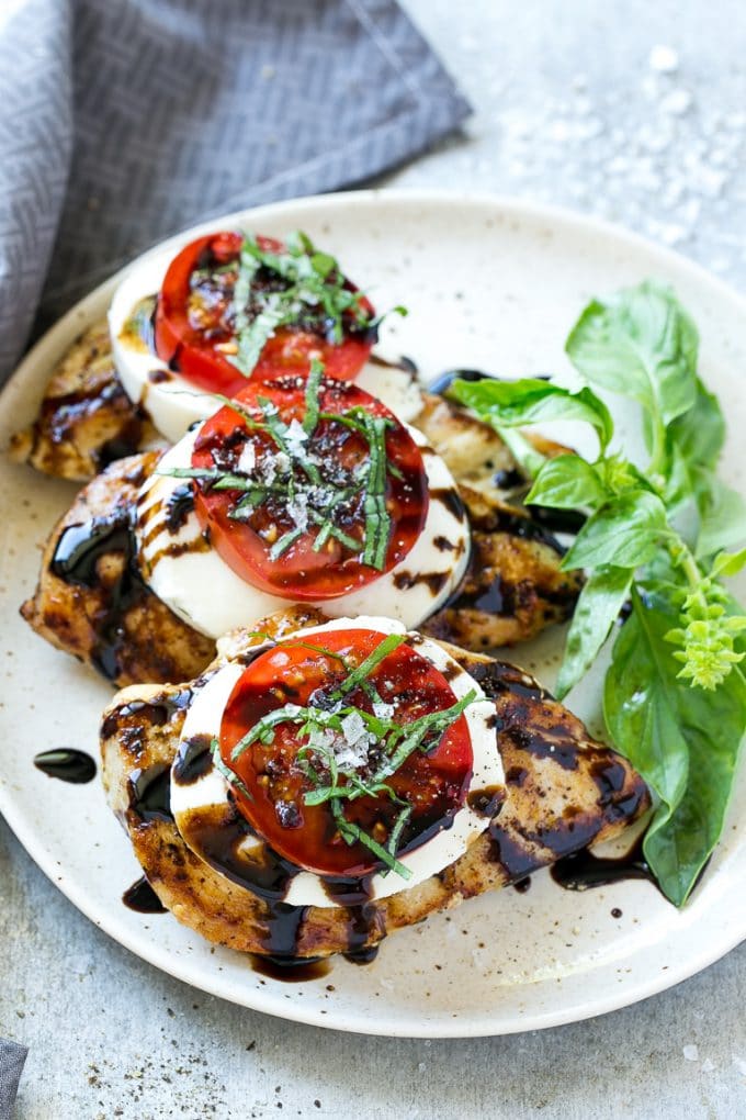 Grilled chicken on a serving plate topped with sliced tomato and cheese.
