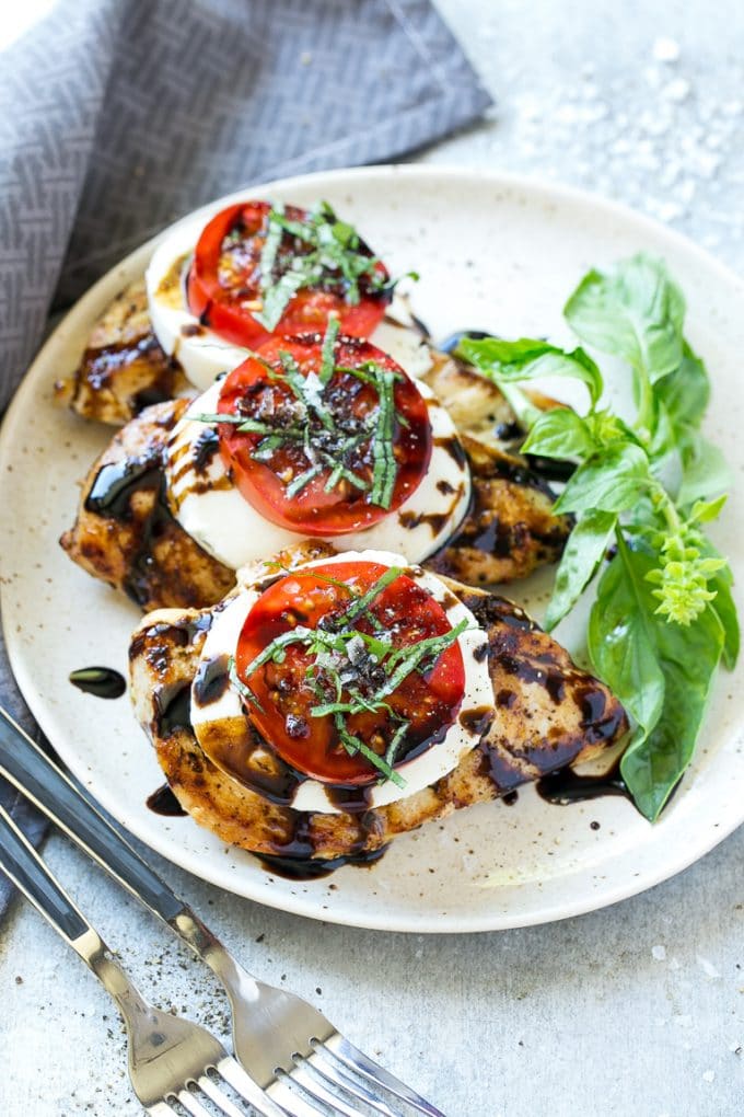 A plate of caprese chicken breasts topped with fresh mozzarella cheese, tomatoes and basil.