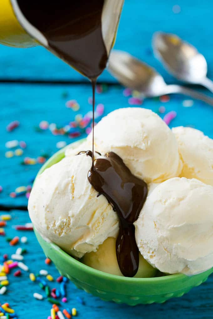 A pitcher of chocolate sauce being poured over vanilla ice cream.