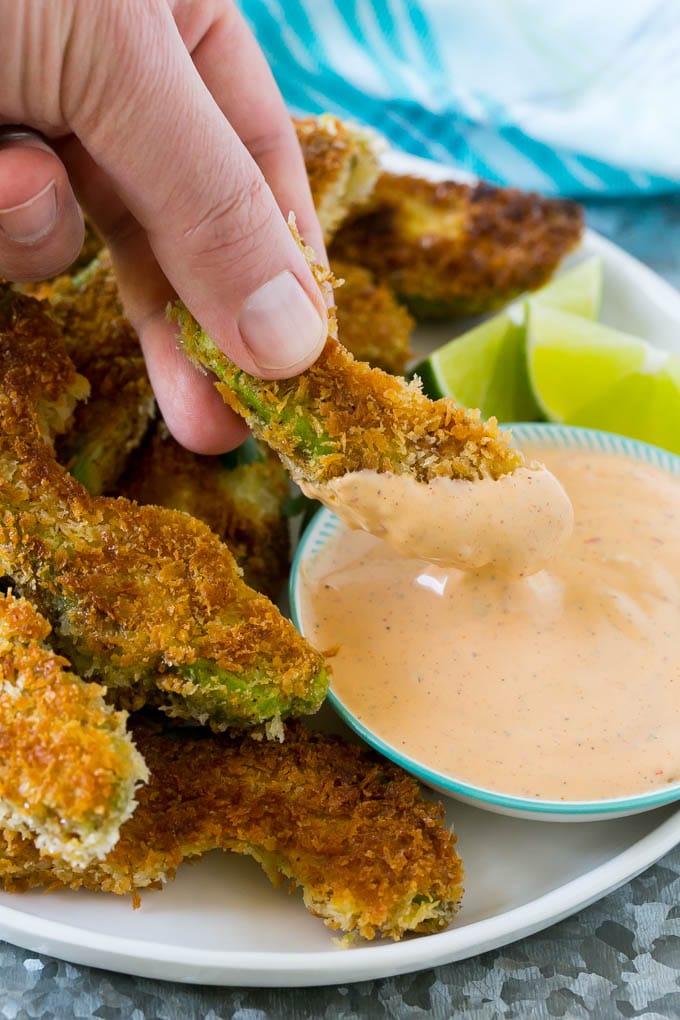 Avocado Fries Recipe | Fried Avocado | Avocado Fritters #avocado #appetizer #snack #fuyos A hand dipping an avocado fry into sauce.