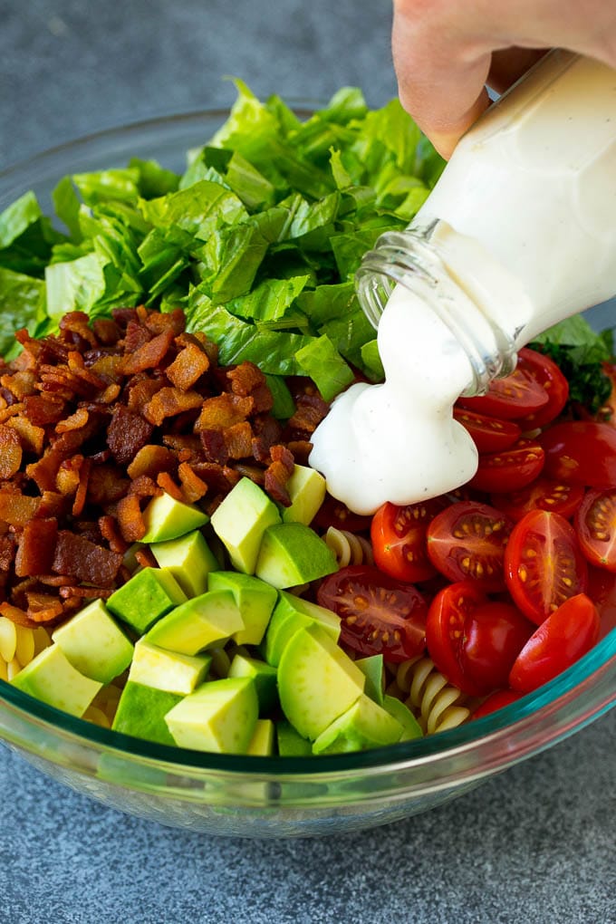 BLT Pasta Salad Recipe | Easy Pasta Salad | Bacon Pasta Salad #salad #pasta #blt #bacon #avocado #dinner #fuyos Ranch dressing being poured over tomatoes, lettuce, bacon and avocado.