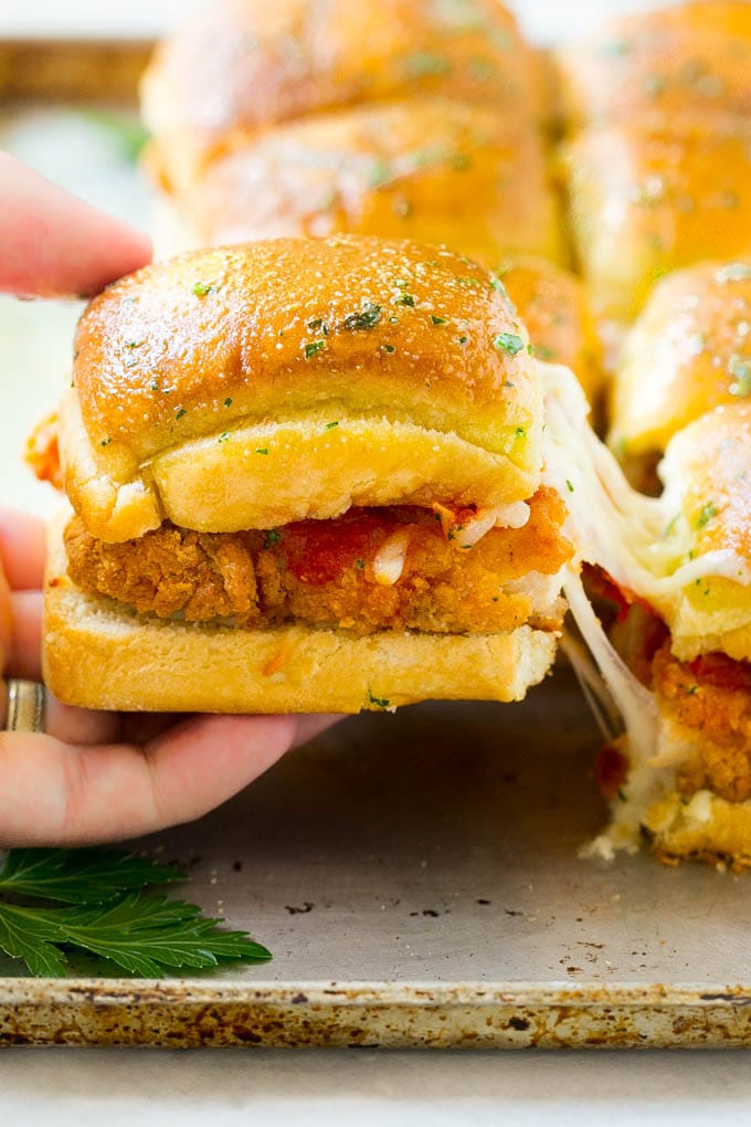 Chicken Parmesan Sliders | Chicken Parmesan Sandwich Recipe | Slider Sandwich Recipe #sliders #chickenparm #chickenparmesan #chickenparmesansliders #dinner #appetizer #fuyos A crispy chicken parmesan slider being pulled away by a hand.