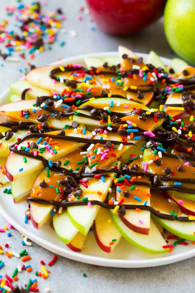 Apple Nachos Recipe | After School Snack | Caramel Apples #apple #apples #caramelapple #snack #dessert #fuyos A plate of red and green sliced apples drizzled with caramel and chocolate, then topped with rainbow sprinkles and chocolate chips.