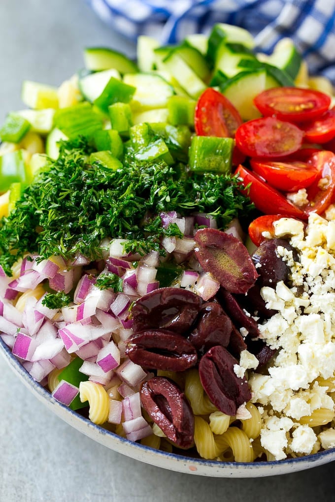 Greek Pasta Salad | Easy Pasta Salad | Vegetable Pasta Salad #pasta #salad #greek #cucumber #tomato #vegetarian #dinner #fuyos A bowl of pasta with red onion, kalamata olives, bell pepper and tomatoes, with a drizzle of Greek dressing.