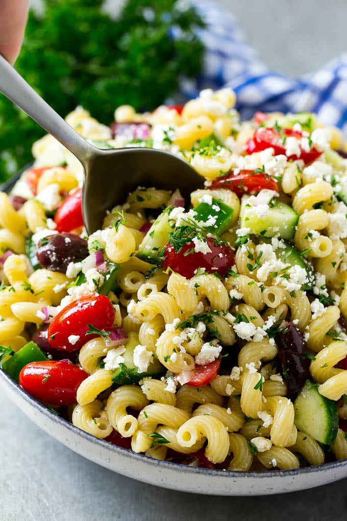 Greek Pasta Salad | Easy Pasta Salad | Vegetable Pasta Salad #pasta #salad #greek #cucumber #tomato #vegetarian #dinner #fuyos A bowl of Greek pasta salad with a serving spoon in it.
