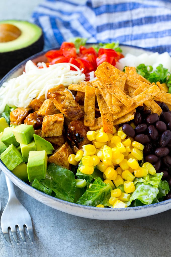 BBQ Chicken Salad Recipe | Chopped BBQ Chicken Salad | CPK Copycat Recipe | California Pizza Kitchen Copycat Recipe | Chicken Ranch Salad #copycat #CPK #BBQchicken #chicken #salad #dinner #fuyos A bowl of salad topped with chicken, tortilla strips, black beans, jiacama, avocado and tomatoes.
