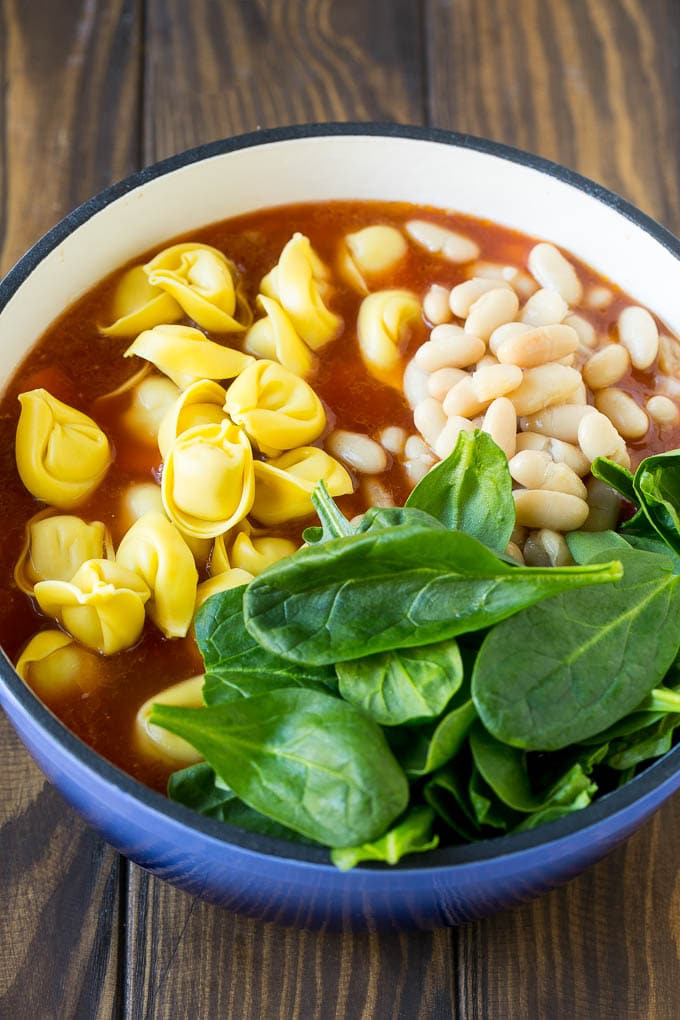 Tortellini Soup Recipe | Sausage Soup | Italian Soup #soup #sausage #pasta #tortellini #dinner #fuyos A pot with ingredients like spinach leaves and white beans.