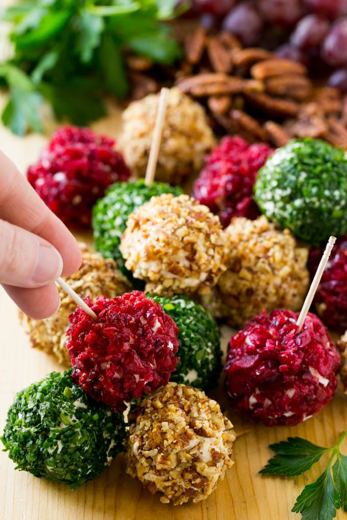 Cheese Ball Bites Recipe | Holiday Cheese Ball Recipe | Pecan Cheese Ball | Cranberry Cheese Ball | Mini Cheese Balls #cheeseball #cheese #appetizer #fuyos A hand reaching for an appetizer crusted in dried craberries.