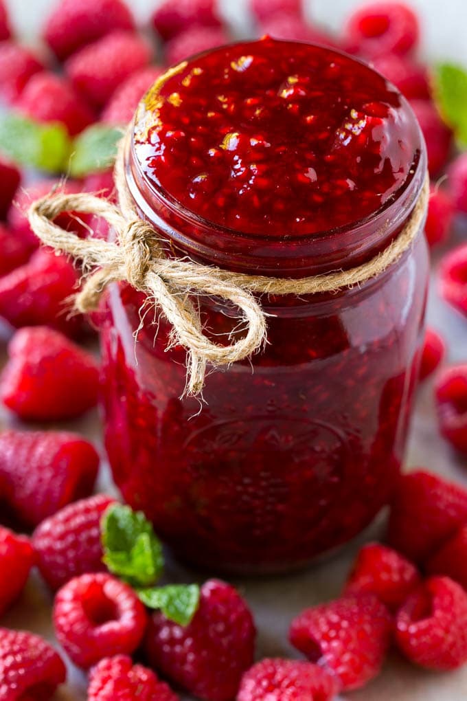 Raspberry Sauce Recipe | Homemade Raspberry Sauce | Raspberry Recipe #raspberries #dessert #fuyos A jar of homemade raspberry sauce surrounded by fresh raspberries.
