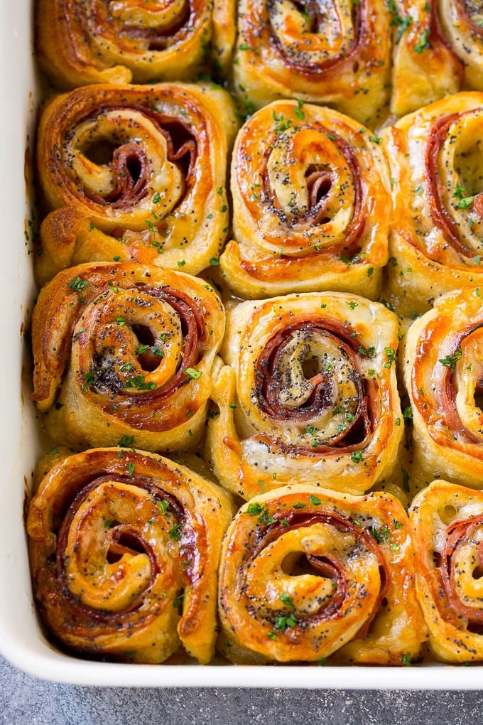 Ham and Cheese Pinwheels Recipe | Ham and Cheese Roll Ups | Ham and Cheese Rolls | Ham and Cheese Bread Rolls #ham #cheese #appetizer #pinwheels #fuyos Ham and cheese pinwheels in a baking dish topped with parsley.