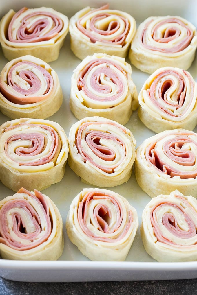 Ham and Cheese Pinwheels Recipe | Ham and Cheese Roll Ups | Ham and Cheese Rolls | Ham and Cheese Bread Rolls #ham #cheese #appetizer #pinwheels #fuyos Rolled up ham, cheese and pizza dough circles in a baking dish.