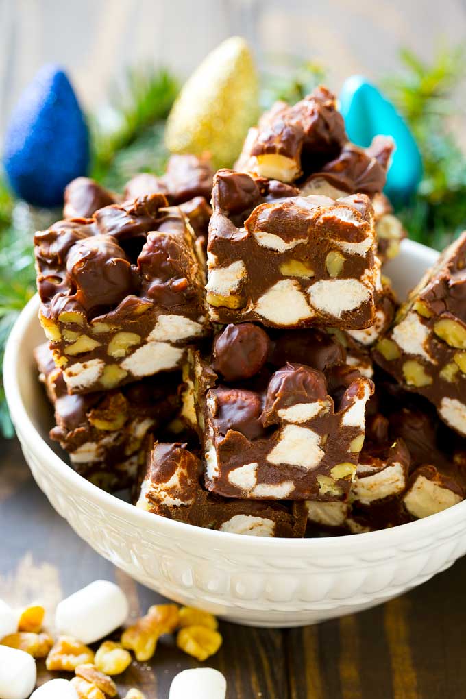 Rocky Road Fudge | Chocolate Marshmallow Fudge | Chocolate Nut Fudge | Microwave Fudge #fudge #chocolatefudge #nobake #chocolate #dessert #rockyroad #fuyos A bowl of fudge squares with holiday decorations in the background.