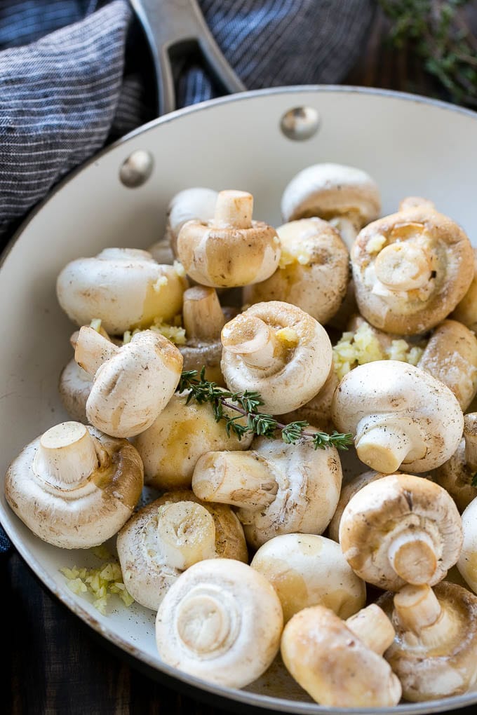 Uncooked buttons with herbs and butter in a frying pan.