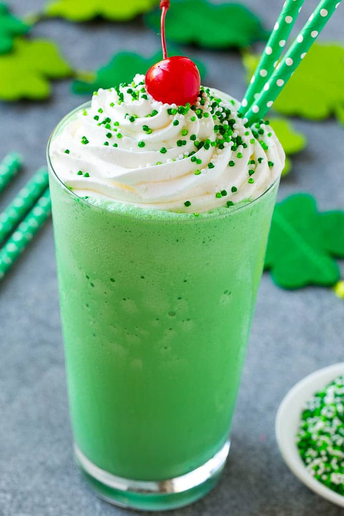 Shamrock Shake Recipe | McDonald's Shamrock Shake | Saint Patrick's Day Drink | Mint Milkshake #milkshake #stpatricksday #saintpatricksday #mint #fuyos A glass of shamrock shake topped with whipped cream, sprinkles and a cherry.