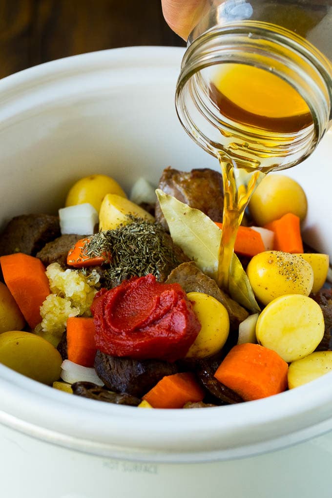 Slow Cooker Beef Stew Recipe | Crockpot Beef Stew #stew #soup #beef #slowcooker #crockpot #dinner #fuyos Broth being poured into a slow cooker filled with beef and vegetables.