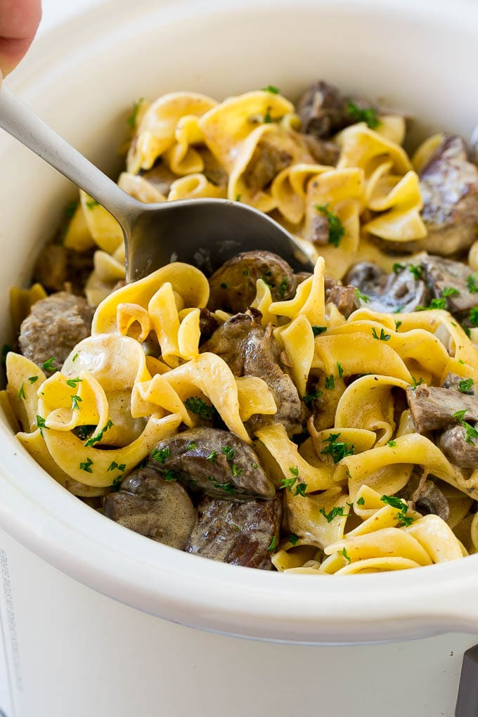 Slow Cooker Beef Stroganoff Recipe | Crock Pot Beef Stroganoff | Beef Recipe #slowcooker #crockpot #beef #mushrooms #pasta #dinner #fuyos A crock pot of beef stroganoff with a serving spoon in it.