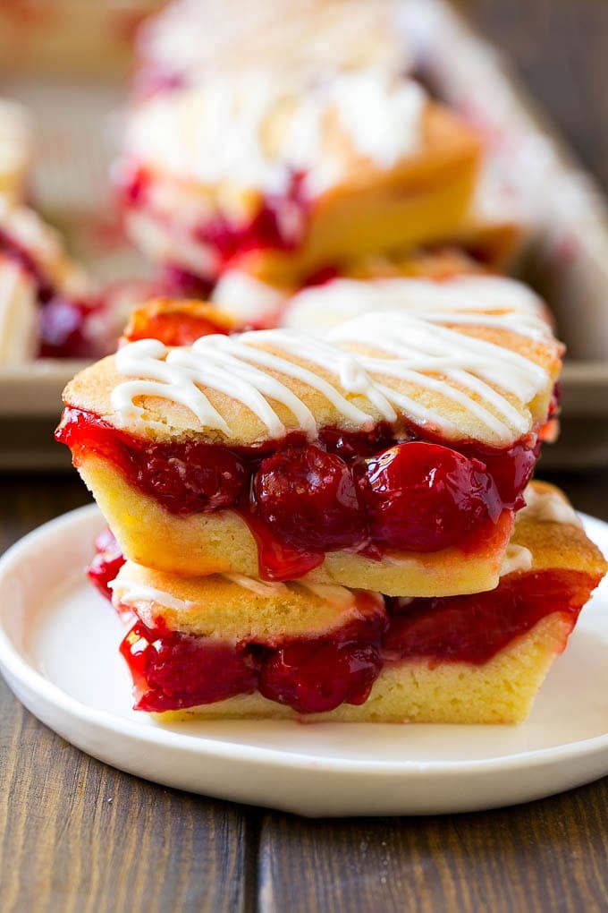 Cherry Bars Recipe | Cherry Pie Bars | Cherry Cookies | Bar Cookies #cookies #bars #cherry #baking #dessert #sweets #fuyos Two cherry bars on a plate with a pan of bars in the background.