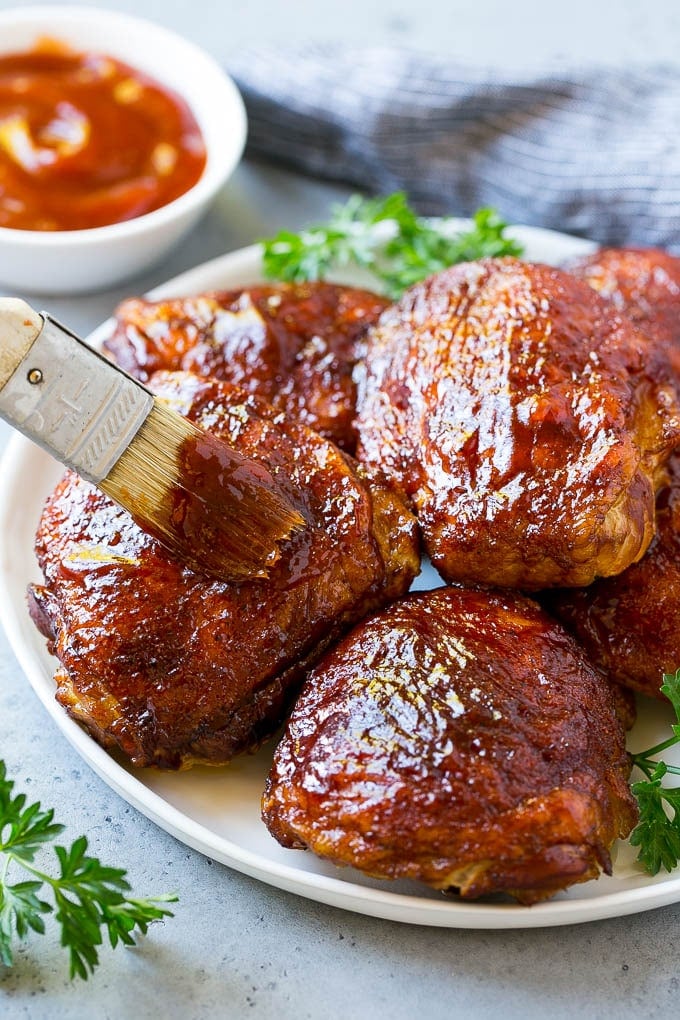 Smoked Chicken Thighs Recipe | Barbecue Chicken Thighs | Easy Chicken Thighs #chicken #barbecue #smoker #dinner #fuyos A plate of smoked chicken thighs being basted with barbecue sauce.