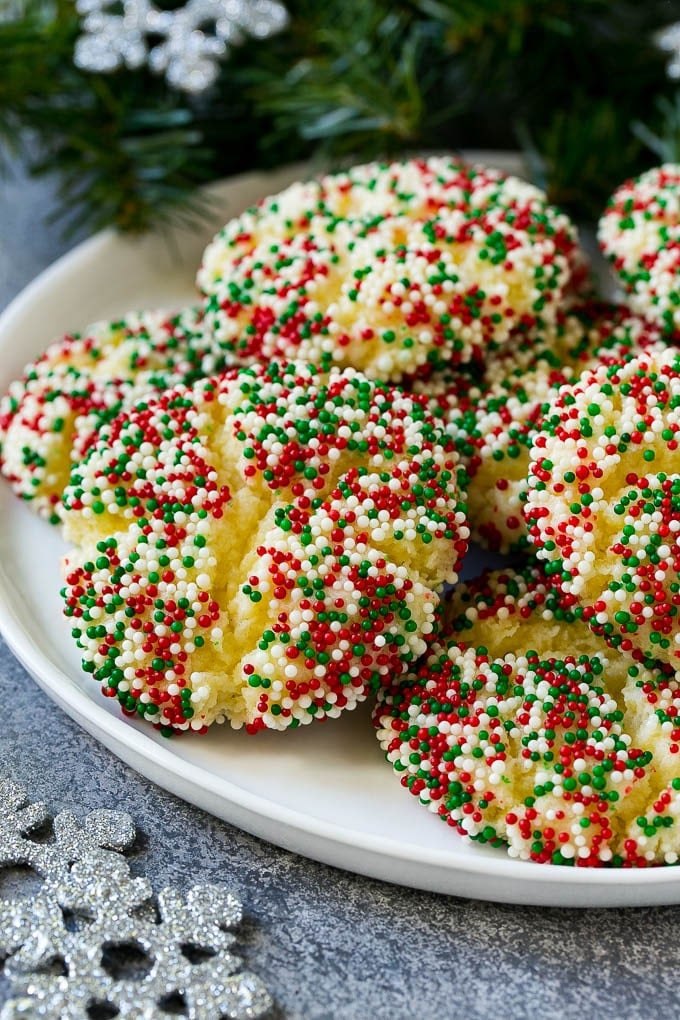 Gooey Butter Cookies Recipe | Cake Mix Cookies | Sprinkle Cookies | Christmas Cookies #cookies #butter #sprinkles #christmas #dessert #baking #fuyos A plate of gooey butter cookies covered in holiday sprinkles.