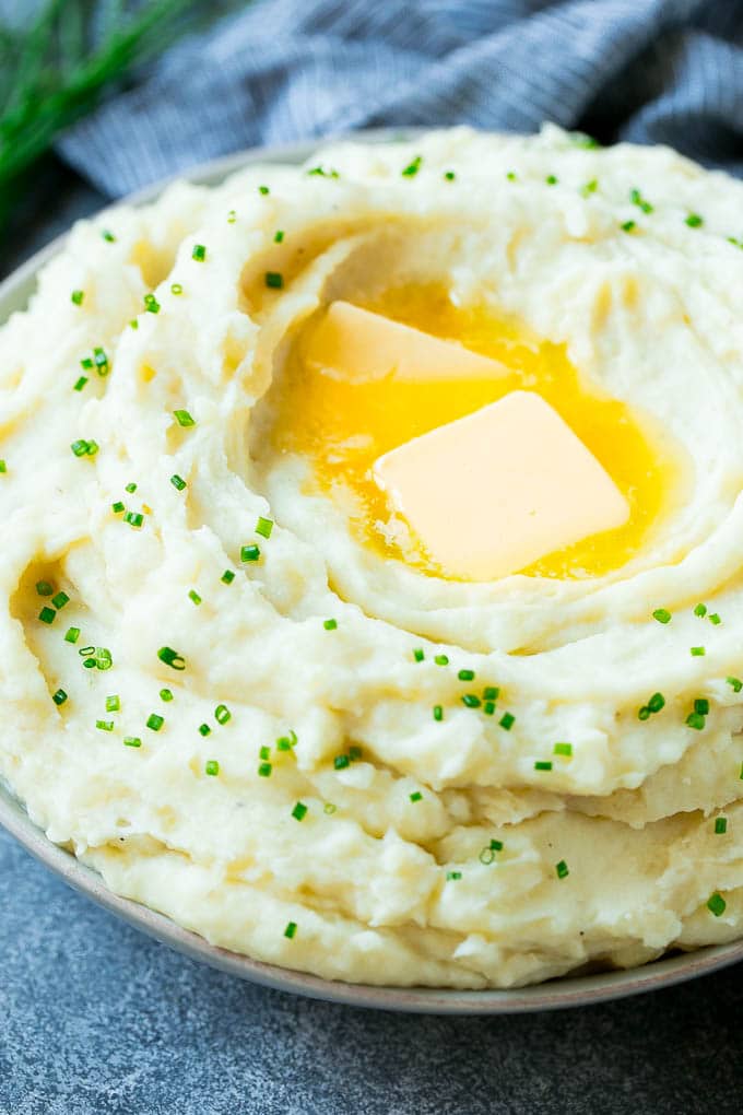 Instant Pot Mashed Potatoes Recipe | Pressure Cooker Mashed Potatoes | Easy Mashed Potatoes #potatoes #sidedish #instantpot #thanksgiving #dinner #fuyos A bowl of fluffy Instant Pot mashed potatoes topped with pats of butter and sliced chives.