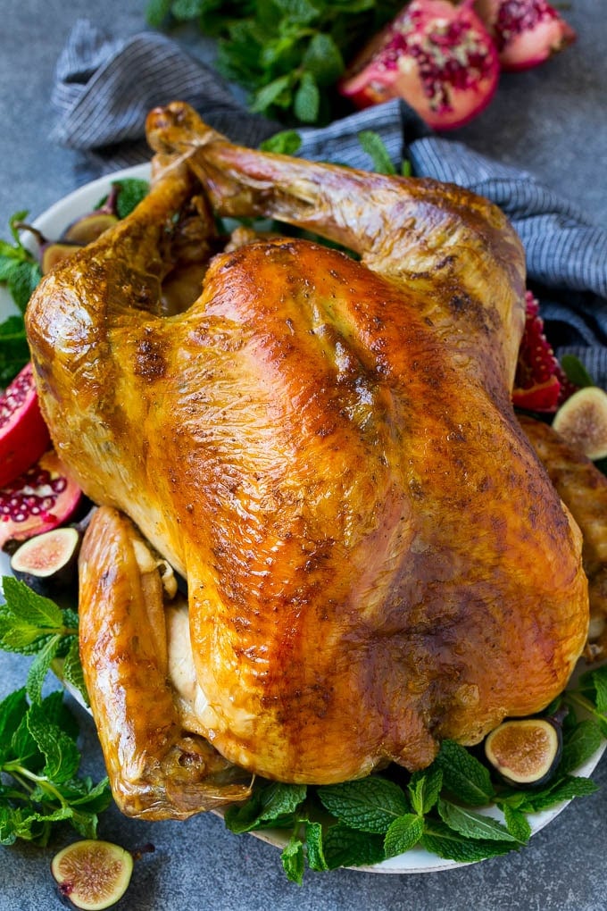 Roast Turkey Recipe | Thanksgiving Turkey | Holiday Turkey | Baked Turkey #turkey #thanksgiving #christmas #dinner #glutenfree #fuyos A Thanksgiving roast turkey on a serving platter garnished with herbs, pomegranate and figs.