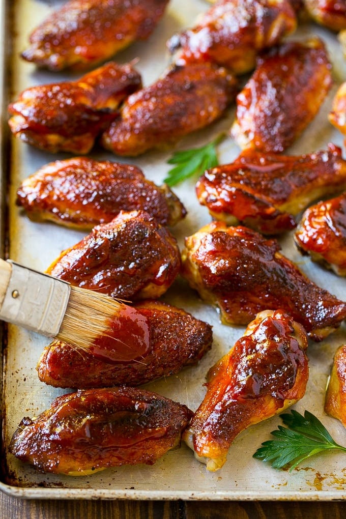 Smoked Chicken Wings | Barbecue Chicken Wings | BBQ Chicken Wings #chicken #wings #bbq #barbecue #appetizer #dinner #fuyos BBQ sauce brushed onto a sheet pan of smoked chicken wings.