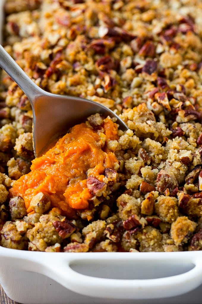 Sweet Potato Casserole with Pecans Recipe | Sweet Potato Casserole | Sweet Potato Side Dish #sweetpotatoes #thanksgiving #pecans #casserole #sidedish #holiday #fall #fuyos A dish of sweet potato casserole with pecans with a serving spoon in it.
