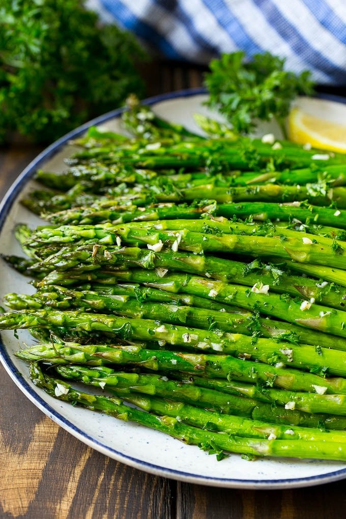 A serving plate of roasted asparagus topped with chopped parsley.