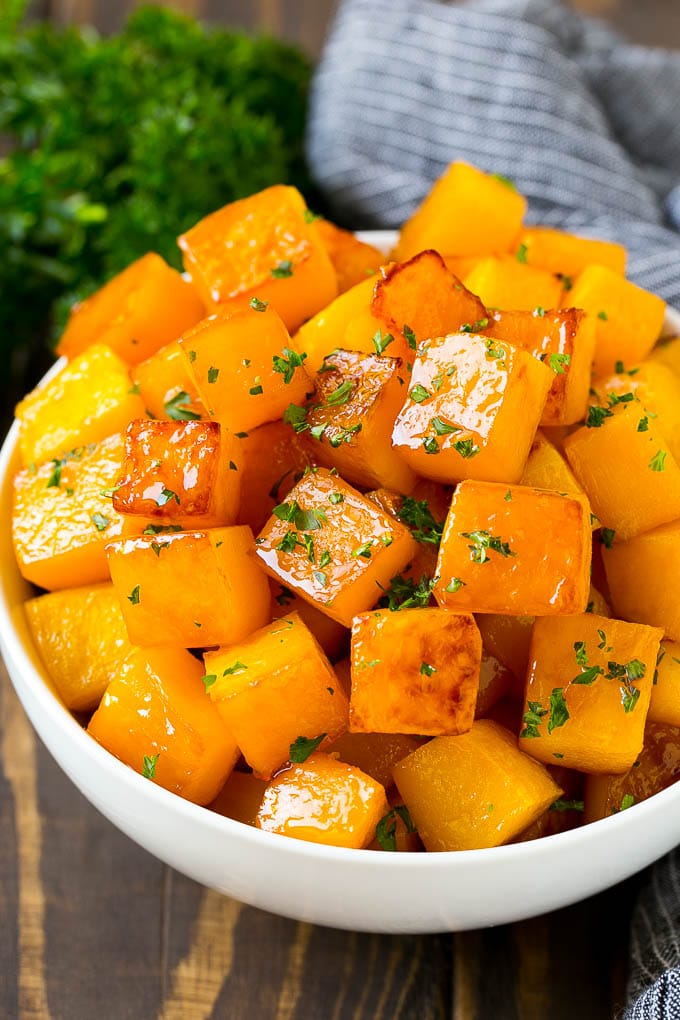 Roasted Butternut Squash Recipe | Baked Butternut Squash | Butternut Squash Side Dish #butternutsquash #squash #fall #vegetarian #dinner #fuyos A bowl of roasted butternut squash made with brown sugar and maple syrup, then garnished with chopped parsley.
