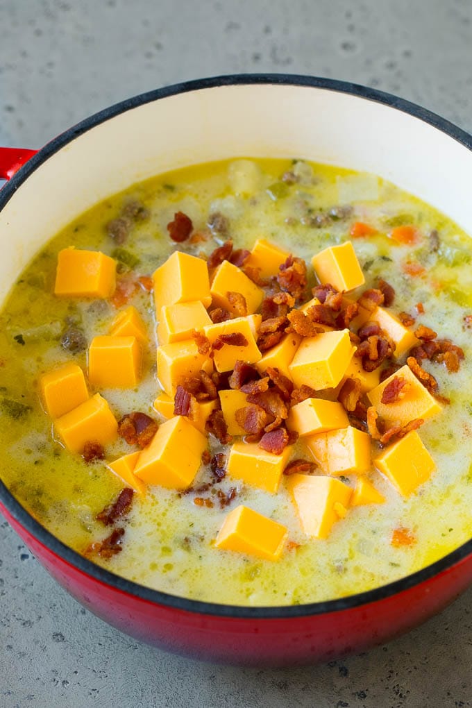 Potato soup base with cubes of Velveeta cheese and bacon being stirred in.