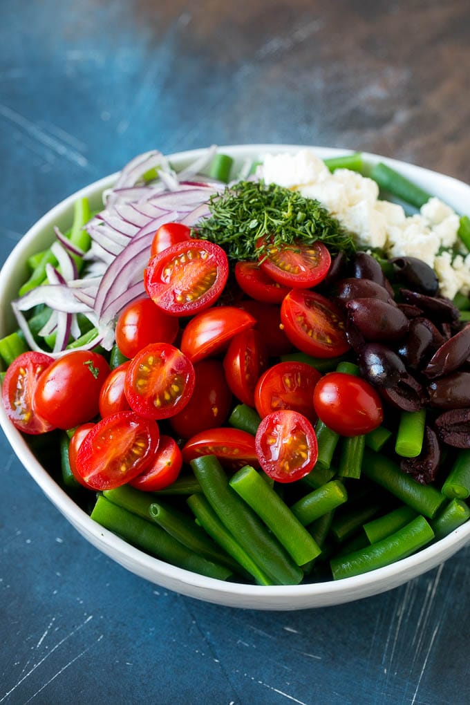 Vegetables like cherry tomatoes, red onion and olives in a bowl with feta cheese.