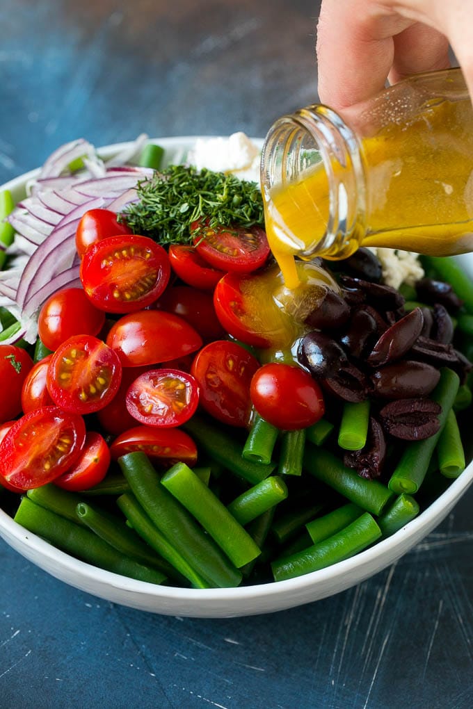 Dressing being poured over veggies like cherry tomatoes, olives and onions.