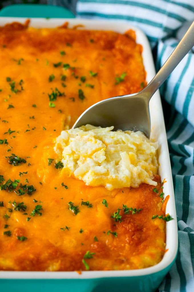 Hash Brown Casserole | Potato Casserole | Hash Brown Side Dish #potatoes #cheese #casserole #sidedish #fuyos Hash brown casserole with potatoes, cheddar cheese, onions and sour cream, with a serving spoon in the dish.