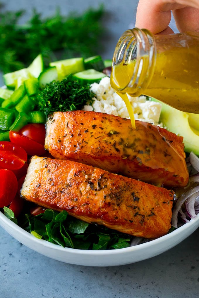 Greek Salmon Salad Recipe | Low Carb Salmon Recipe | Salmon Salad #salmon #seafood #fish #lowcarb #keto #lunch #fuyos #healthy Salmon fillets on top of greens with dressing being poured over the top.