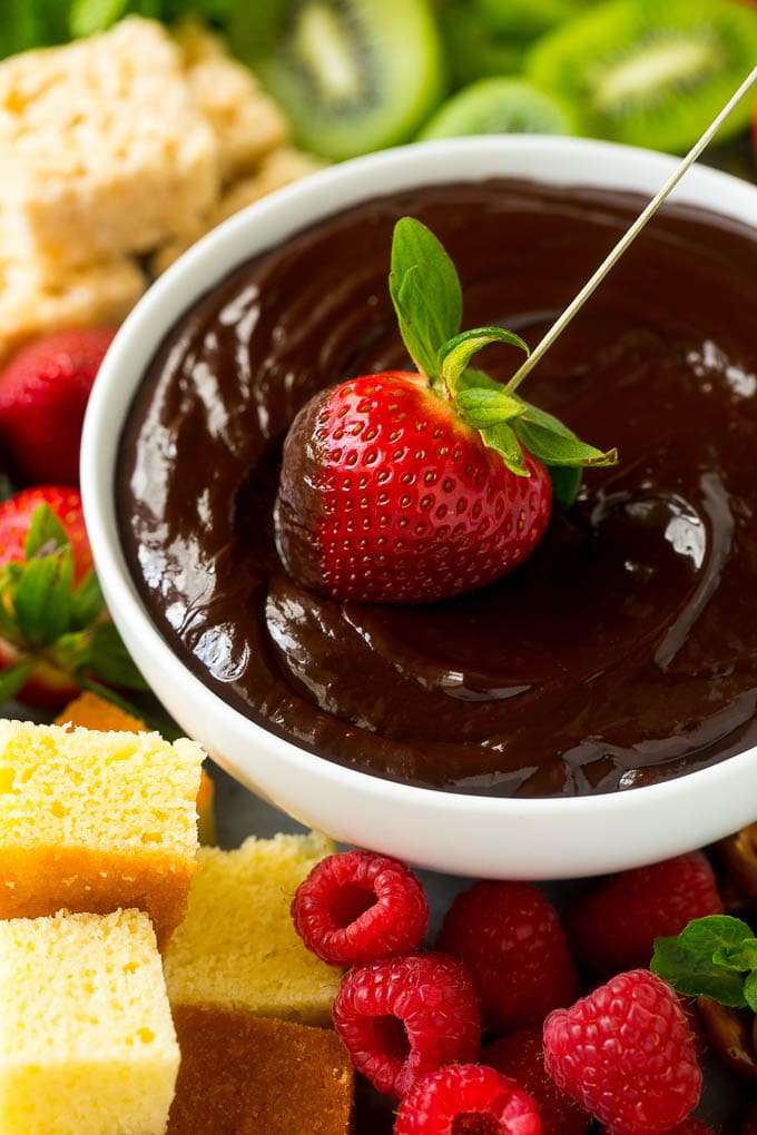A strawberry being dipped into a bowl of fondue.