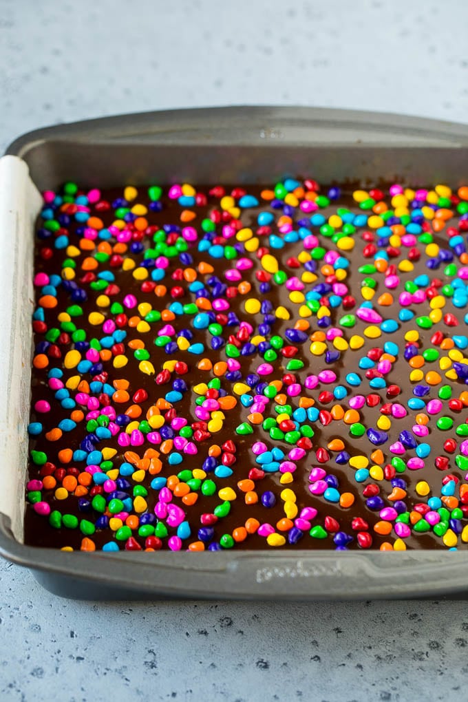 Cosmic Brownies Recipe | Cocoa Brownies | Frosted Brownies #brownies #chocolate #dessert #fuyos #sprinkles A pan of cosmic brownies with rainbow sprinkles on top.