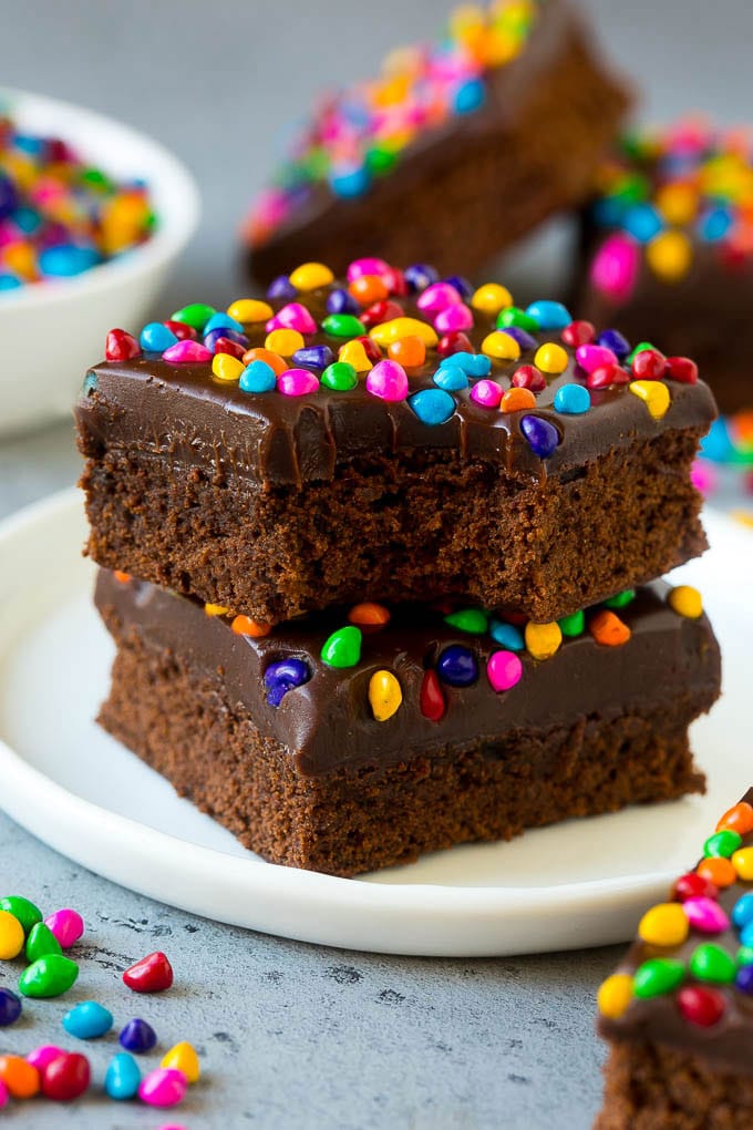 Cosmic Brownies Recipe | Cocoa Brownies | Frosted Brownies #brownies #chocolate #dessert #fuyos #sprinkles A stack of cosmic brownies on a plate with a bite taken out of one.