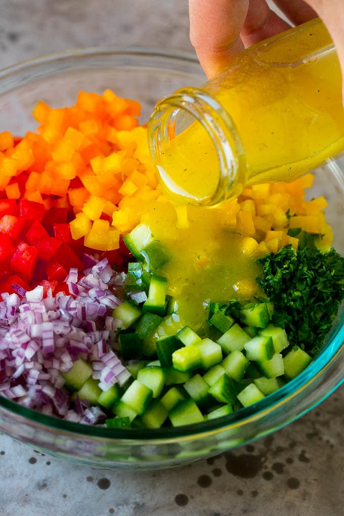 Israeli Salad Recipe | Cucumber Salad | Tomato Salad | Chopped Salad #salad #cleaneating #healthy #glutenfree #lowcarb #keto #sidedish #lunch #fuyos Lemon dressing being poured over chopped vegetables.