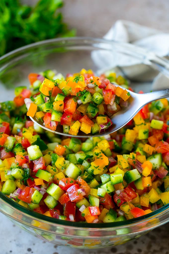 Israeli Salad Recipe | Cucumber Salad | Tomato Salad | Chopped Salad #salad #cleaneating #healthy #glutenfree #lowcarb #keto #sidedish #lunch #fuyos A spoon holding up a serving of Israeli salad.