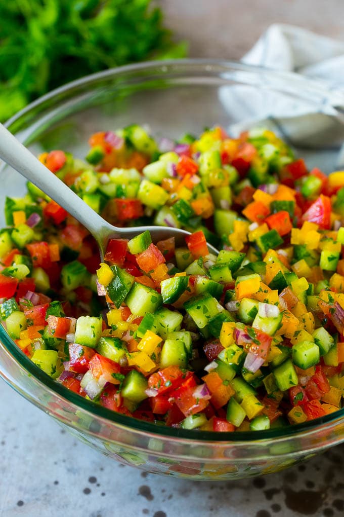 Israeli Salad Recipe | Cucumber Salad | Tomato Salad | Chopped Salad #salad #cleaneating #healthy #glutenfree #lowcarb #keto #sidedish #lunch #fuyos A bowl of Israeli salad with a serving spoon in it.