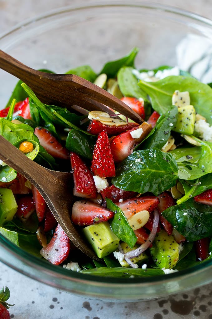 Salad tongs in a bowl of spinach salad with strawberries.