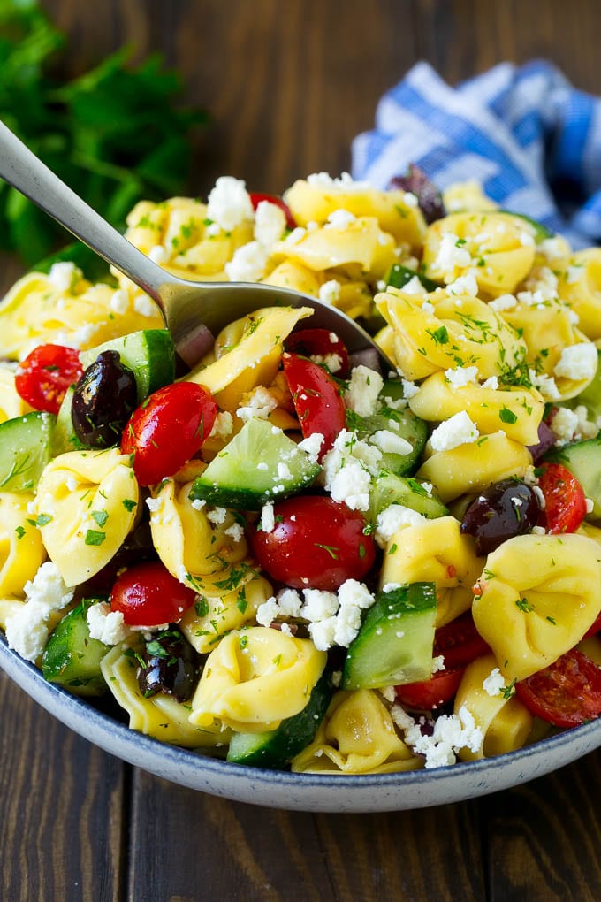 Greek Tortellini Salad Recipe | Pasta Salad | Tortellini Salad | Greek Salad #greek #tortellini #pasta #salad #cucumbers #olives #dinner #fuyos A bowl of Greek tortellini salad with a serving spoon in it.
