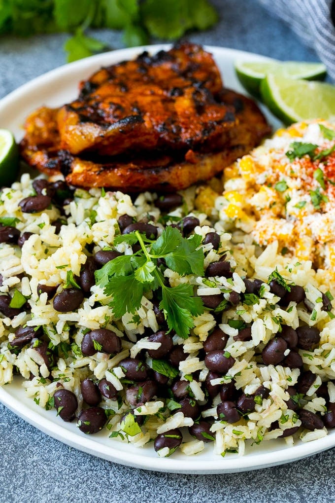 A plate of black beans and rice with grilled pork and Mexican corn.