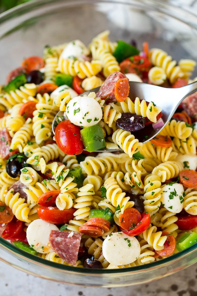 Italian Pasta Salad | Pasta Salad Recipe #pasta #salad #pastasalad #pepperoni #salami #olives #cheese #sidedish #fuyos A serving spoon in a bowl of Italian style pasta salad.