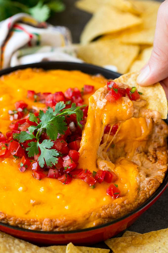 Bean Dip Recipe | Mexican Dip #dip #appetizer #mexicanfood #beans #cheese #fuyos A tortilla chip scooping out a serving of Mexican bean dip.
