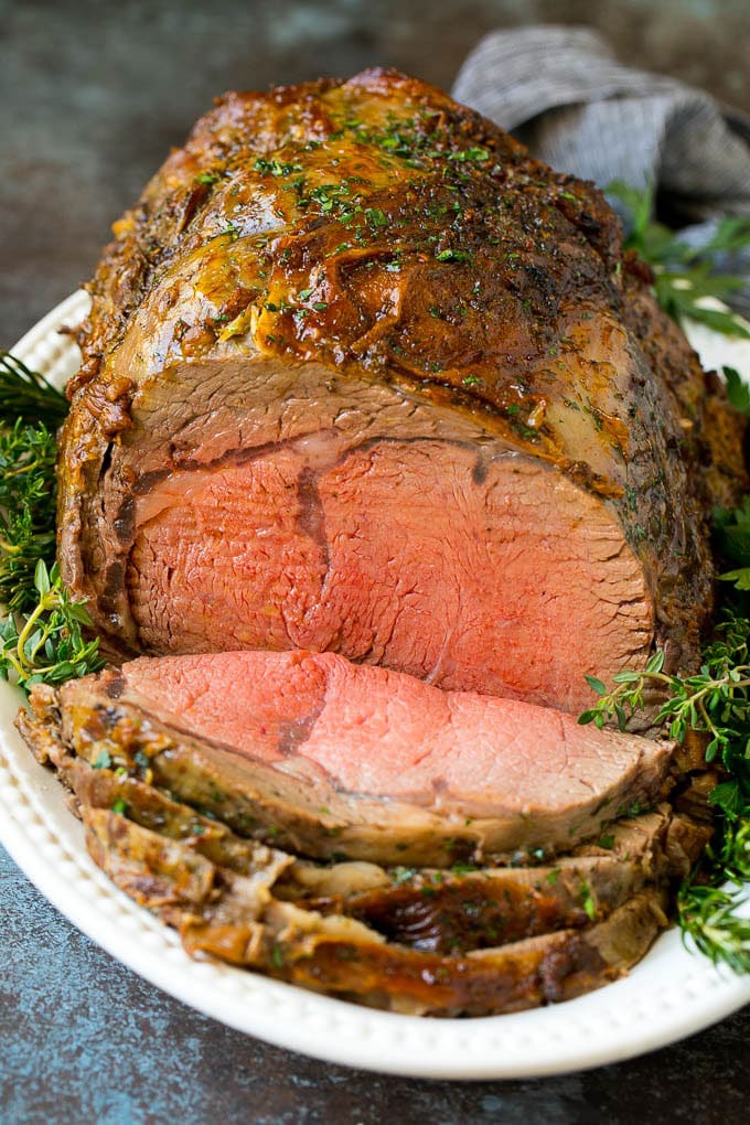 Prime Rib Recipe #primerib #beef #roast #dinner #thanksgiving #christmas #keto #lowcarb #fuyos A sliced slow roasted prime rib roast surrounded by fresh herbs.