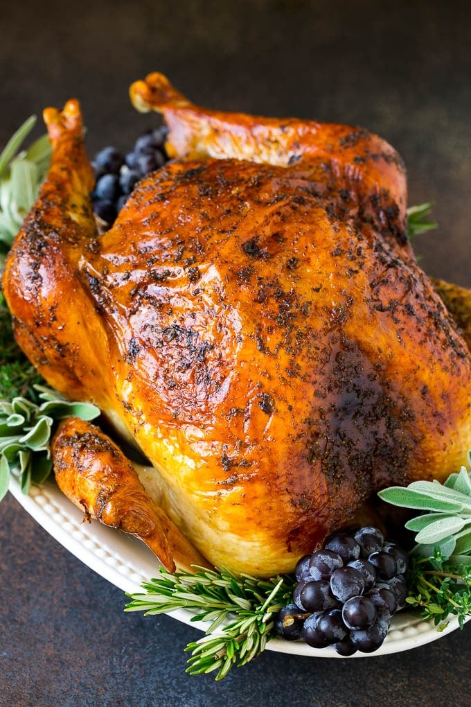 Thanksgiving Turkey Recipe | Roasted Turkey #turkey #thanksgiving #fall #dinner #fuyos A whole roasted Thanksgiving turkey on a platter that's decorated with grapes and herbs.